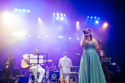 Woman in blue dress singing on stage in front of Royal Australian Navy Band