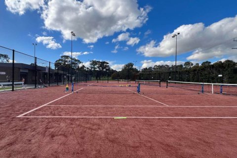 Fenced tennis courts with floodlights surrounded by trees